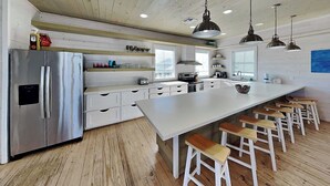 A modern kitchen with a large island, white cabinetry, and wooden stools. - Bella Vista by Silver Sands Vacation Rentals (Port Aransas)