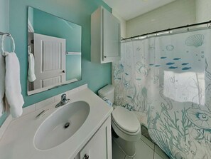 A bathroom with a sink, mirror, toilet, and a shower curtain with a sea-themed design.