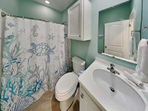 A bathroom with a sea turtle shower curtain, a white toilet, a sink with a mirror, and a towel rack.