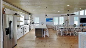 A modern kitchen with a central island, white cabinetry, and a dining area with white chairs. - Bella Vista by Silver Sands Vacation Rentals (Port Aransas)