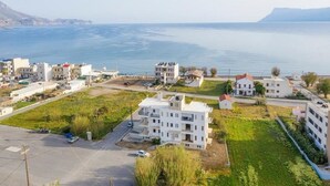 A coastal residential area with modern buildings, a parking lot, and a view of the sea.