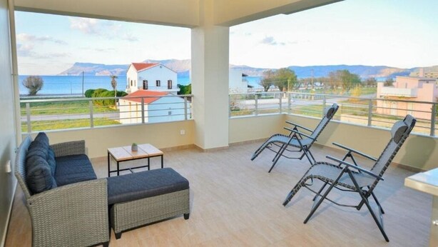 A balcony with wicker furniture, a view of the sea, and a building in the background.