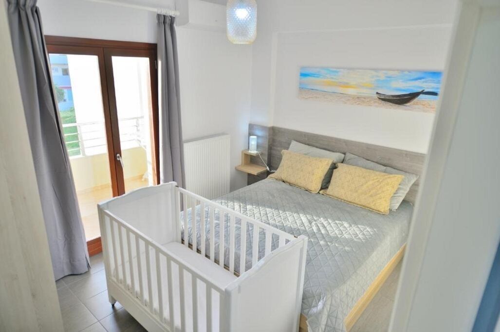 Un dormitorio con una cama, una cuna blanca, un cuadro de una playa y vistas a un balcón.