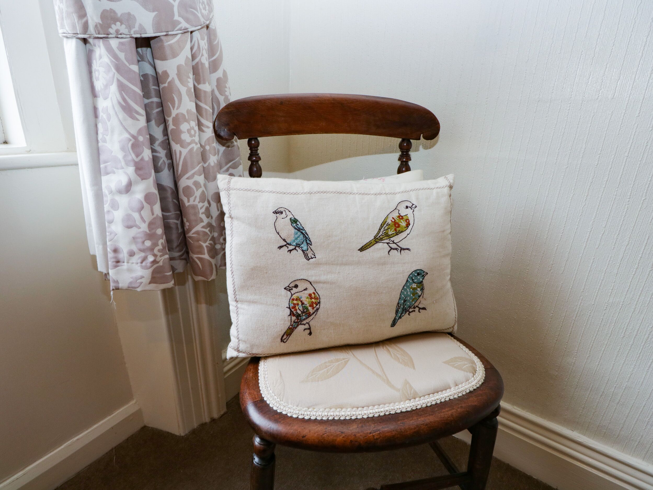 Une chaise en bois avec un coussin orné d’oiseaux brodés.