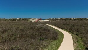 A pathway leading to a beach area with a wooden structure. - Buried Treasure by Silver Sands Vacation Rentals (Port Aransas)
