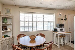 A compact kitchen with a dining table, chairs, a microwave, and a small refrigerator. - Buried Treasure by Silver Sands Vacation Rentals (Port Aransas)