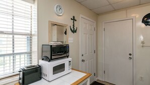 A kitchenette with a microwave, toaster, and a clock on the wall. - Buried Treasure by Silver Sands Vacation Rentals (Port Aransas)