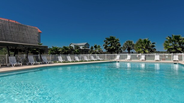 A swimming pool with lounge chairs and a building with a red roof. - Buried Treasure by Silver Sands Vacation Rentals (Port Aransas)
