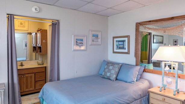 A bedroom with a bed, a nightstand, a mirror, and a wardrobe. - Buried Treasure by Silver Sands Vacation Rentals (Port Aransas)