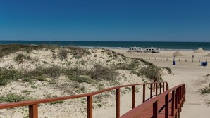 A beach with a wooden boardwalk leading to a sandy area with RVs parked. - Buried Treasure by Silver Sands Vacation Rentals (Port Aransas)