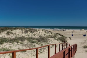 A beach with a wooden boardwalk leading to a sandy area with RVs parked. - Buried Treasure by Silver Sands Vacation Rentals (Port Aransas)
