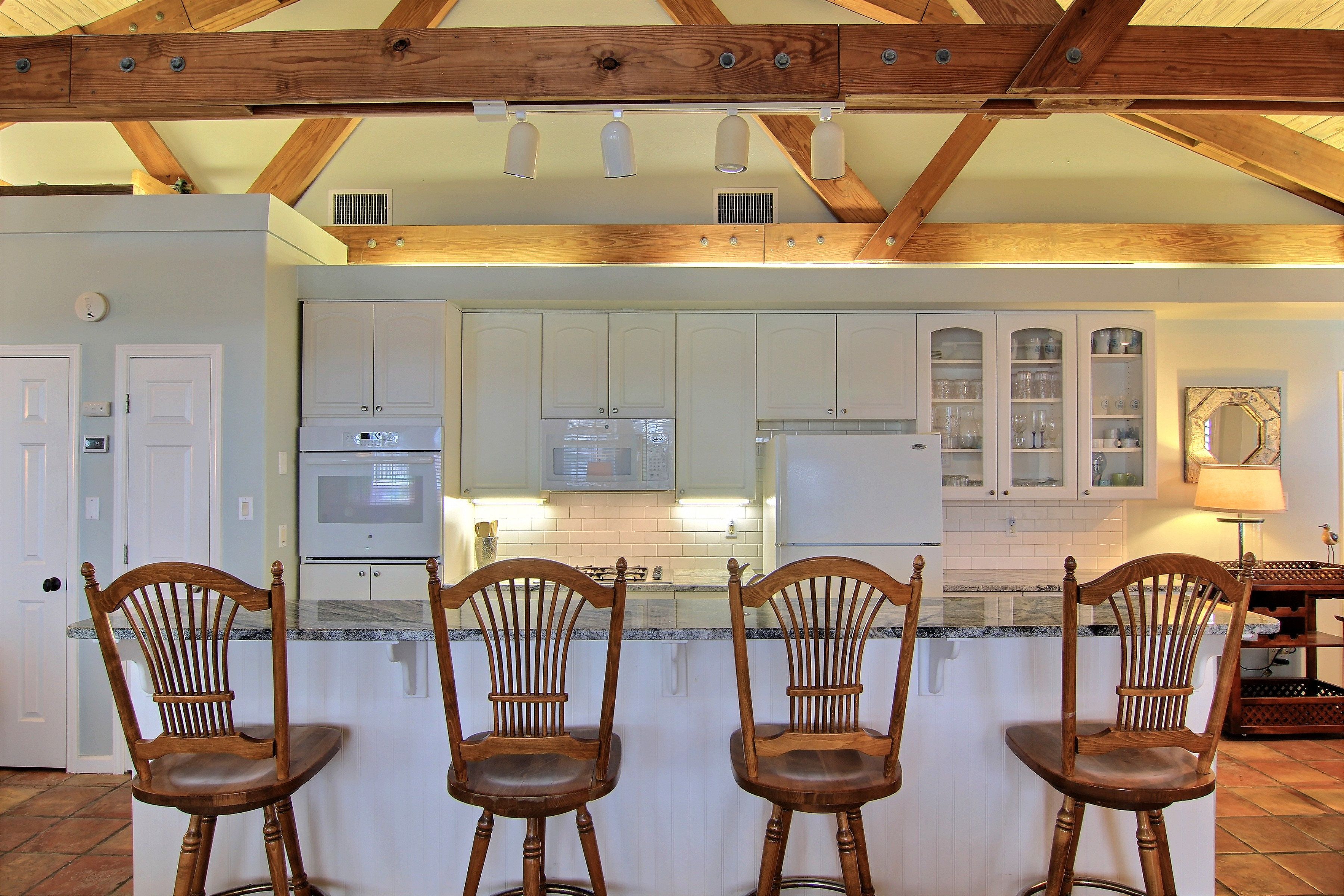 A kitchen with wooden beams, white cabinets, and a bar area with three wooden bar stools.