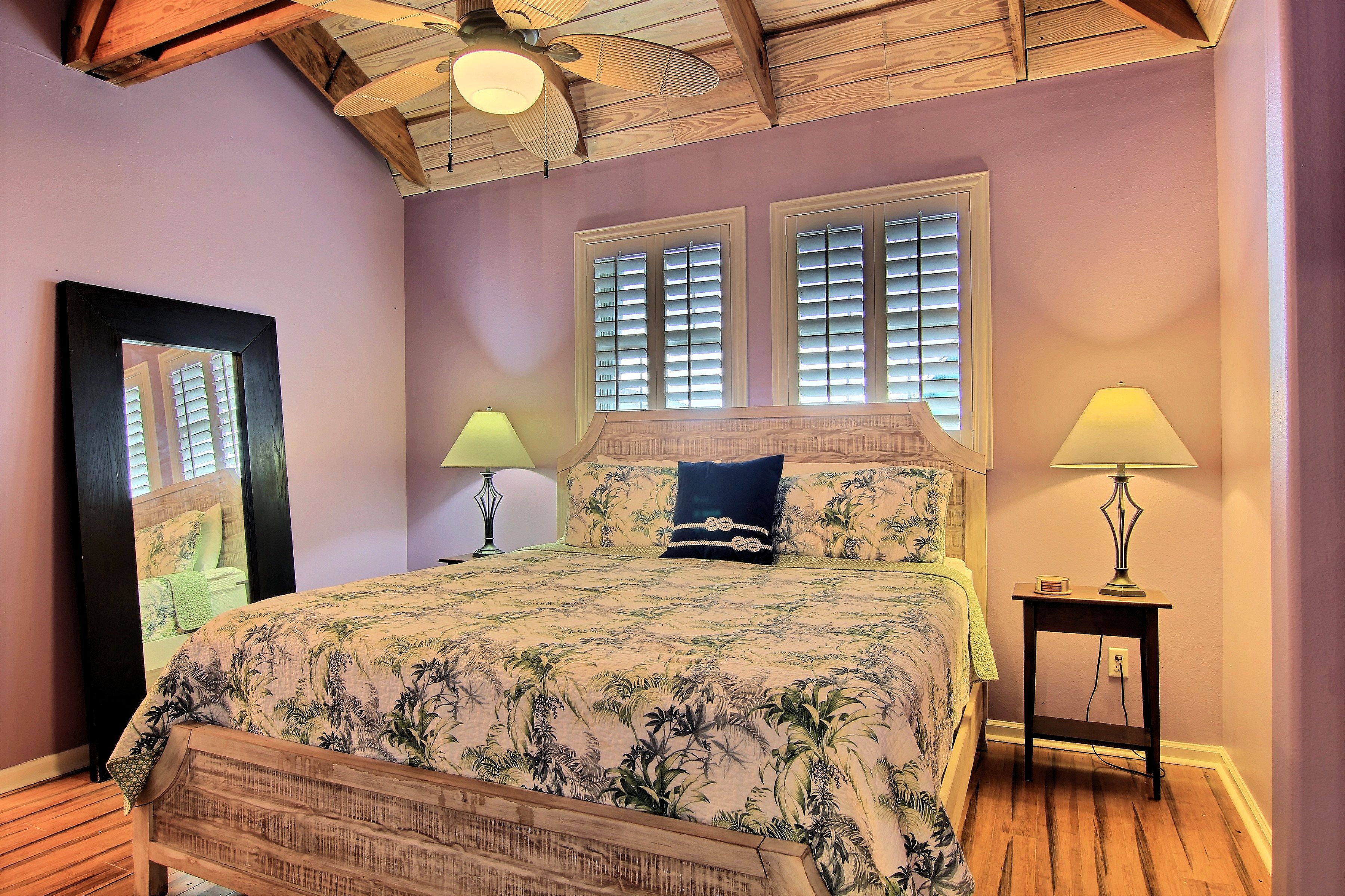 Quarto com cama, duas luminárias de cabeceira, ventilador de teto e janela com persianas.