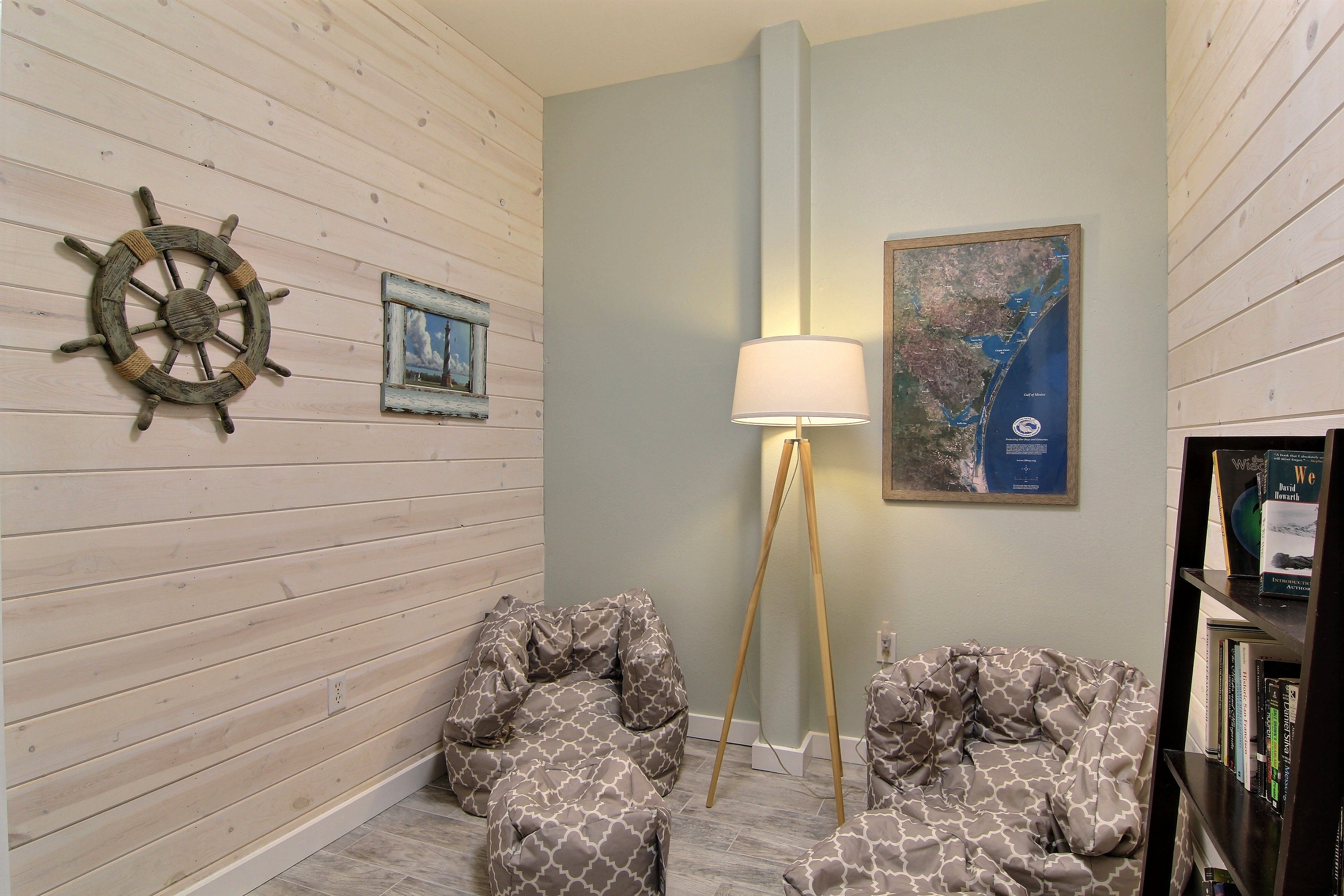 Une pièce aux murs recouverts de panneaux de bois, décorée d’un gouvernail de bateau, ornée d’un tableau encadré, d’un lampadaire et d’une bibliothèque.