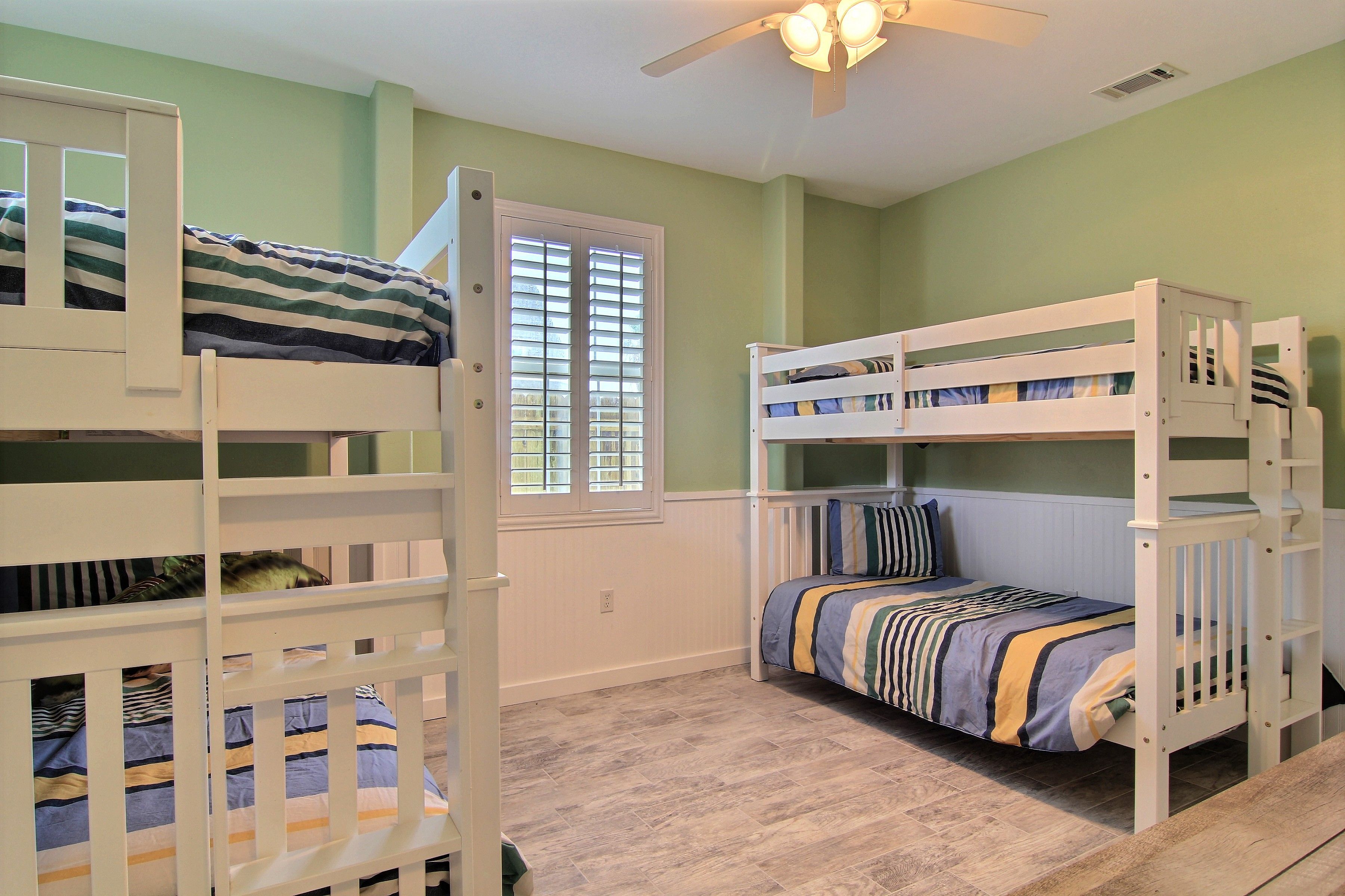 A room with two bunk beds, a window with blinds, a ceiling fan, and a light switch on the wall.