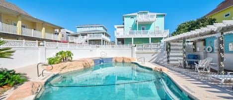 A swimming pool with clear blue water, surrounded by a white fence and a building with multiple balconies.