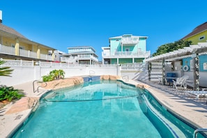 A swimming pool with clear blue water, surrounded by a white fence and a building with multiple balconies.