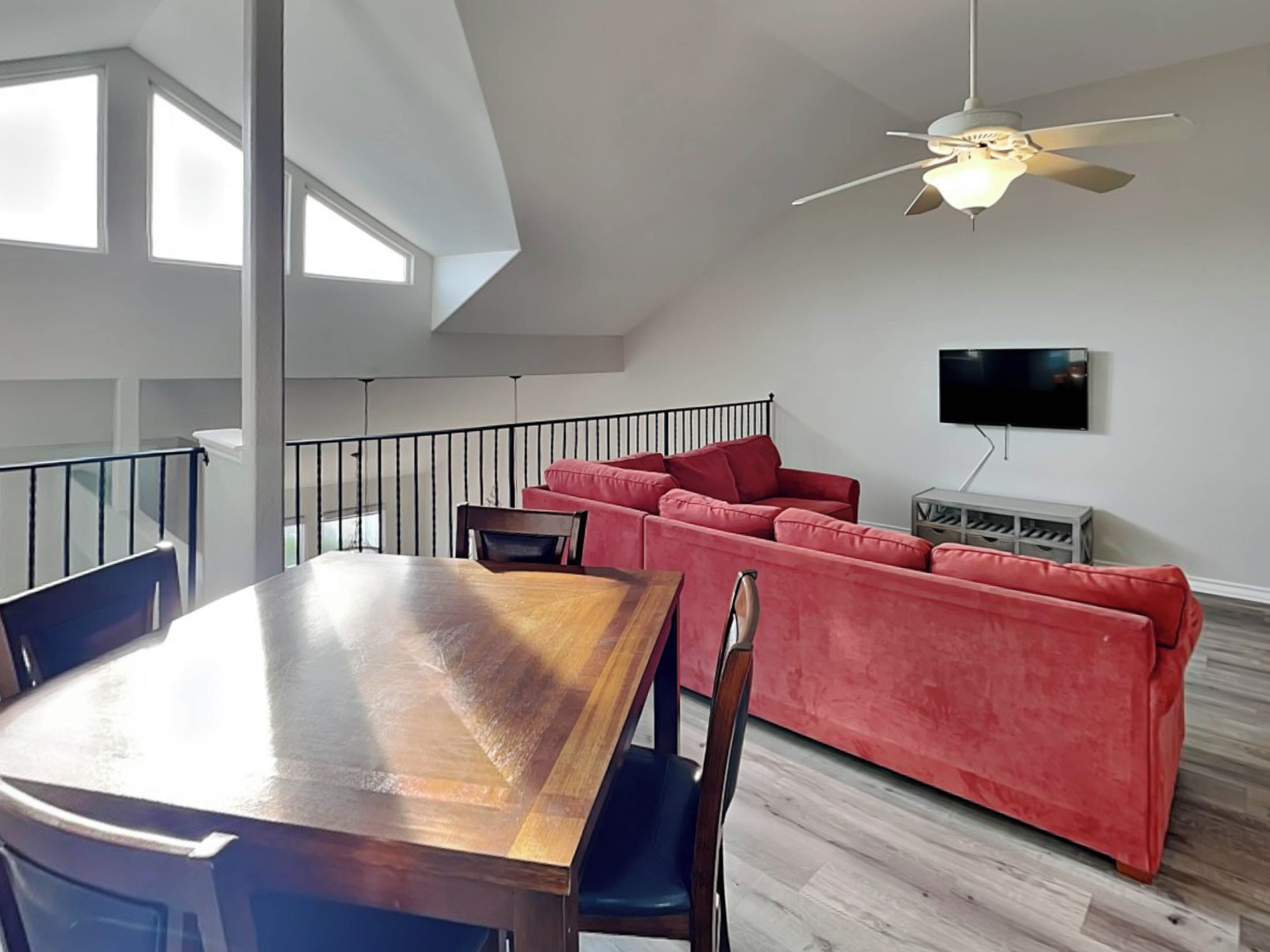 A modern living room with a wooden dining table, red sofa, and a ceiling fan.