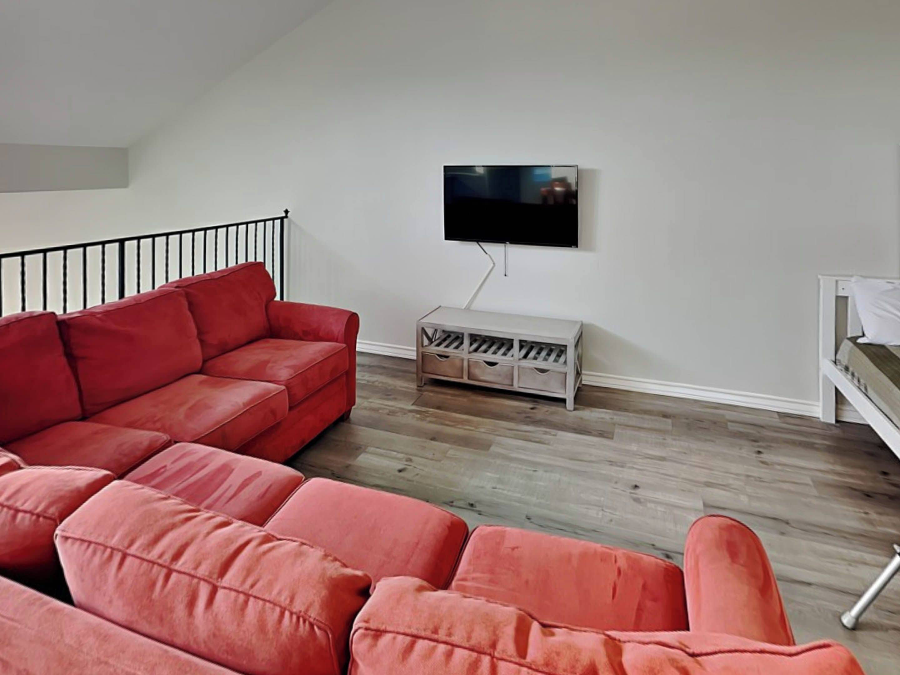 A living room with a red sofa, a TV mounted on the wall, and a wooden floor.