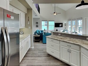 A modern kitchen with white cabinetry, a stainless steel refrigerator, a marble countertop, and a ceiling fan. - Blew By You by Silver Sands Vacation Rentals (Port Aransas)