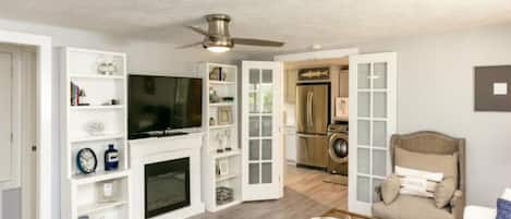 Una sala de estar moderna con chimenea, televisión y comedor, con una cocina al fondo.