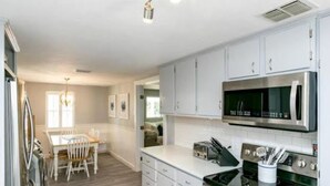 A modern kitchen with white cabinets, a stainless steel microwave, and a gas stove. - Cape Cod Cottage by Silver Sands Vacation Rentals (Port Aransas)