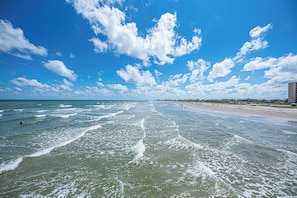 Ein Strand mit Wellen, einem klaren Himmel und Gebäuden in der Ferne.