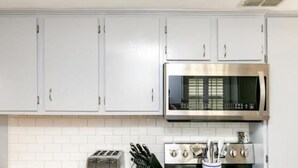 A kitchen with white cabinets, a microwave, a toaster, and a stove. - Cape Cod Cottage by Silver Sands Vacation Rentals (Port Aransas)