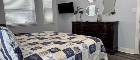 A bedroom with a bed, dresser, two wall-mounted mirrors, and a flat-screen TV.