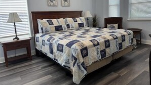 A bedroom with a large bed, two bedside tables, a nightstand, a lamp, and two wall-mounted picture frames. - Coastal Cutie by Silver Sands Vacation Rentals (Port Aransas)