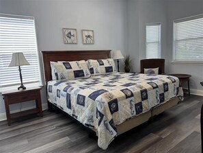 A bedroom with a large bed, two bedside tables, a nightstand, a lamp, and two wall-mounted picture frames.