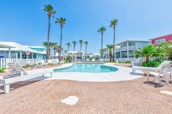 A pool area with white lounge chairs, palm trees, and a clear blue sky.