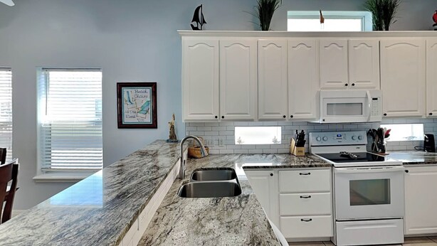 A kitchen with white cabinets, a granite countertop, a sink, a stove, and a microwave. - Coastal Cutie by Silver Sands Vacation Rentals (Port Aransas)