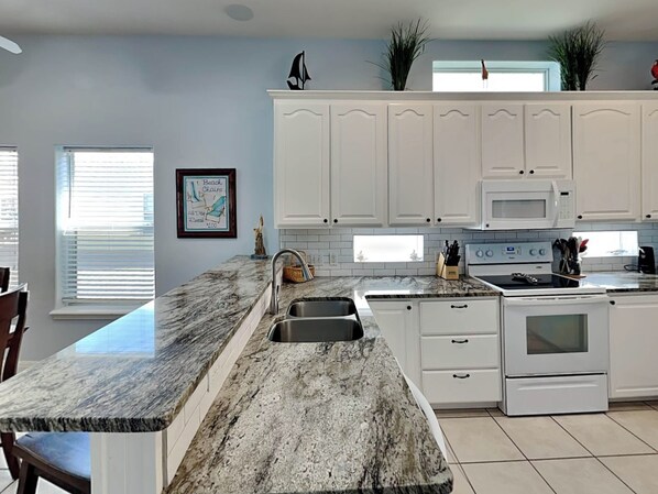 A kitchen with white cabinets, a granite countertop, a sink, a stove, and a microwave.