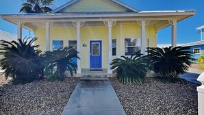 A yellow building with a blue door, white columns, and a covered porch. - Coastal Cutie by Silver Sands Vacation Rentals (Port Aransas)