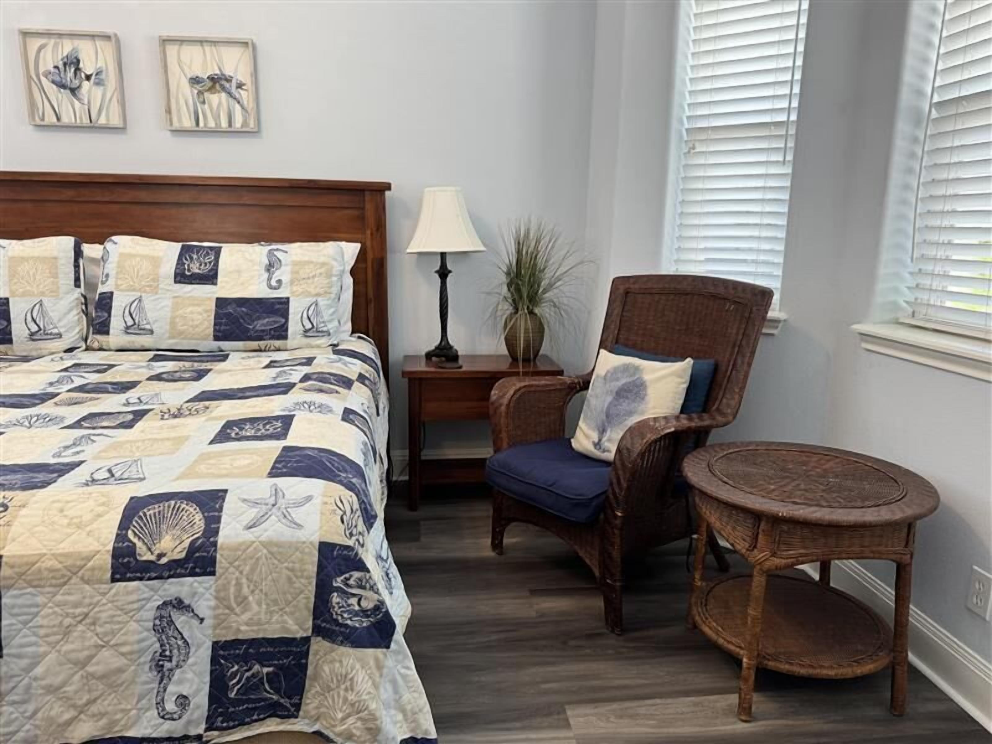 A bedroom with a bed, a chair, a nightstand, a lamp, and a window with blinds.