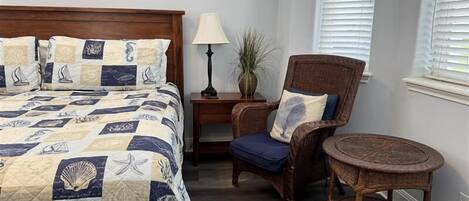 A bedroom with a bed, a chair, a nightstand, a lamp, and a window with blinds.