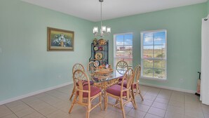 A dining area with a glass table surrounded by wicker chairs, a chandelier, and a window with blinds. - Casa La Vista by Silver Sands Vacation Rentals (Port Aransas)