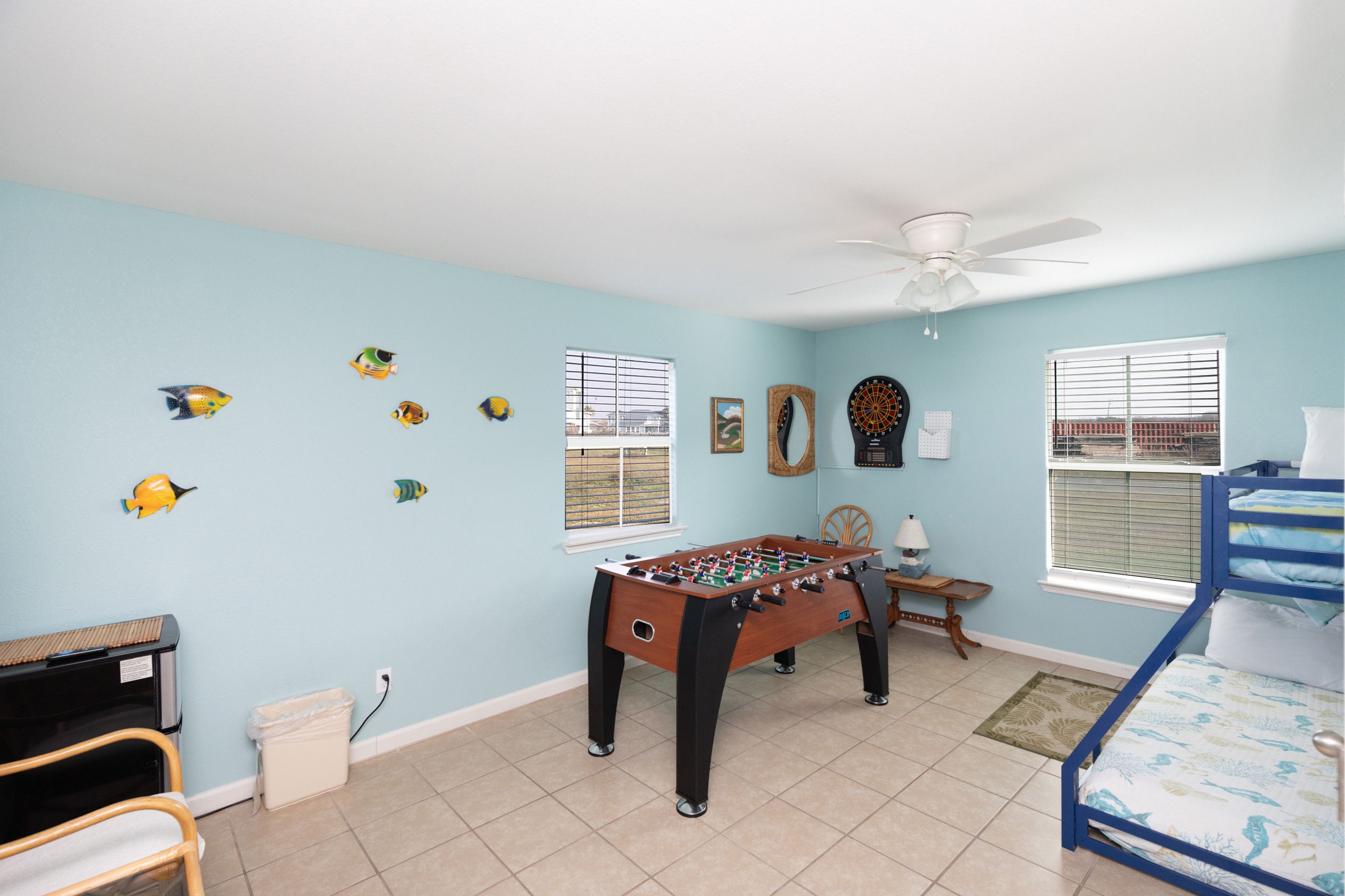 A room with a foosball table, a bed, a desk, and a ceiling fan.