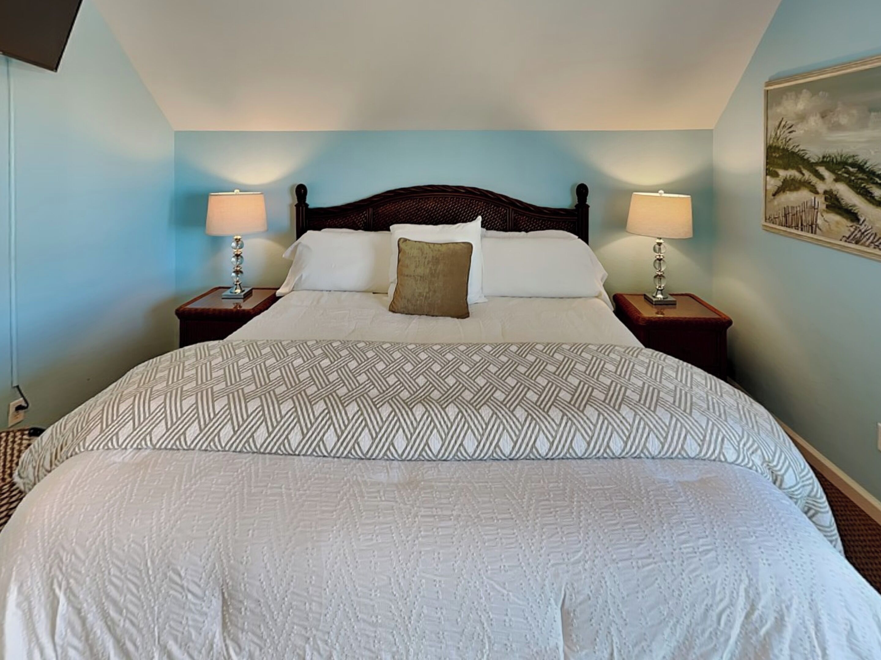 A neatly made bed with a patterned bedspread, two bedside lamps, and a painting on the wall.