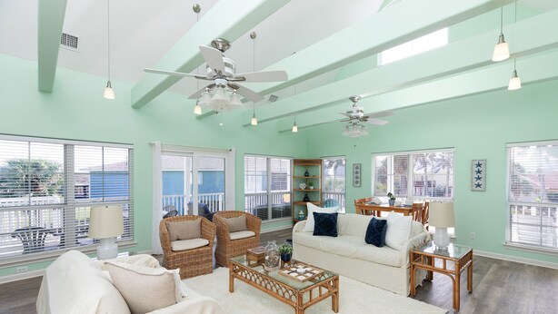 A spacious living room with a high ceiling, large windows, wicker furniture, and ceiling fans. - Casa La Vista by Silver Sands Vacation Rentals (Port Aransas)