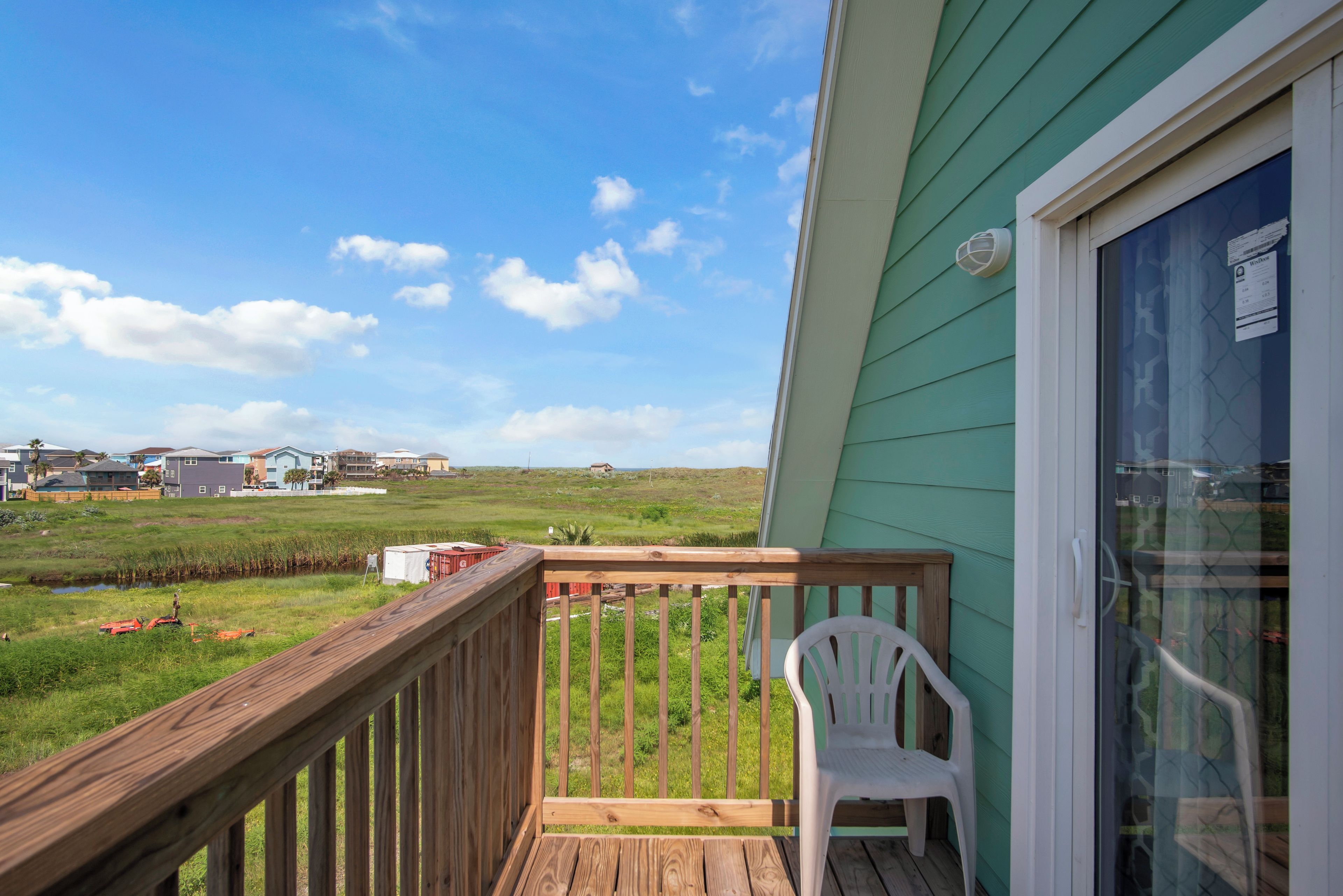 Una terraza de madera con una silla blanca, con vista a un campo cubierto de césped y casas a lo lejos.