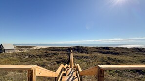 En trätrappa som leder ner till en strand med fri utsikt över havet och det avlägsna landskapet.