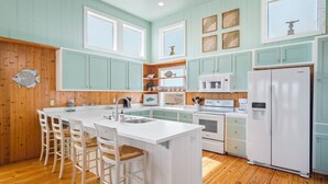 Una cocina con una isla grande, armarios de madera, electrodomésticos blancos y una decoración de pescado en la pared.