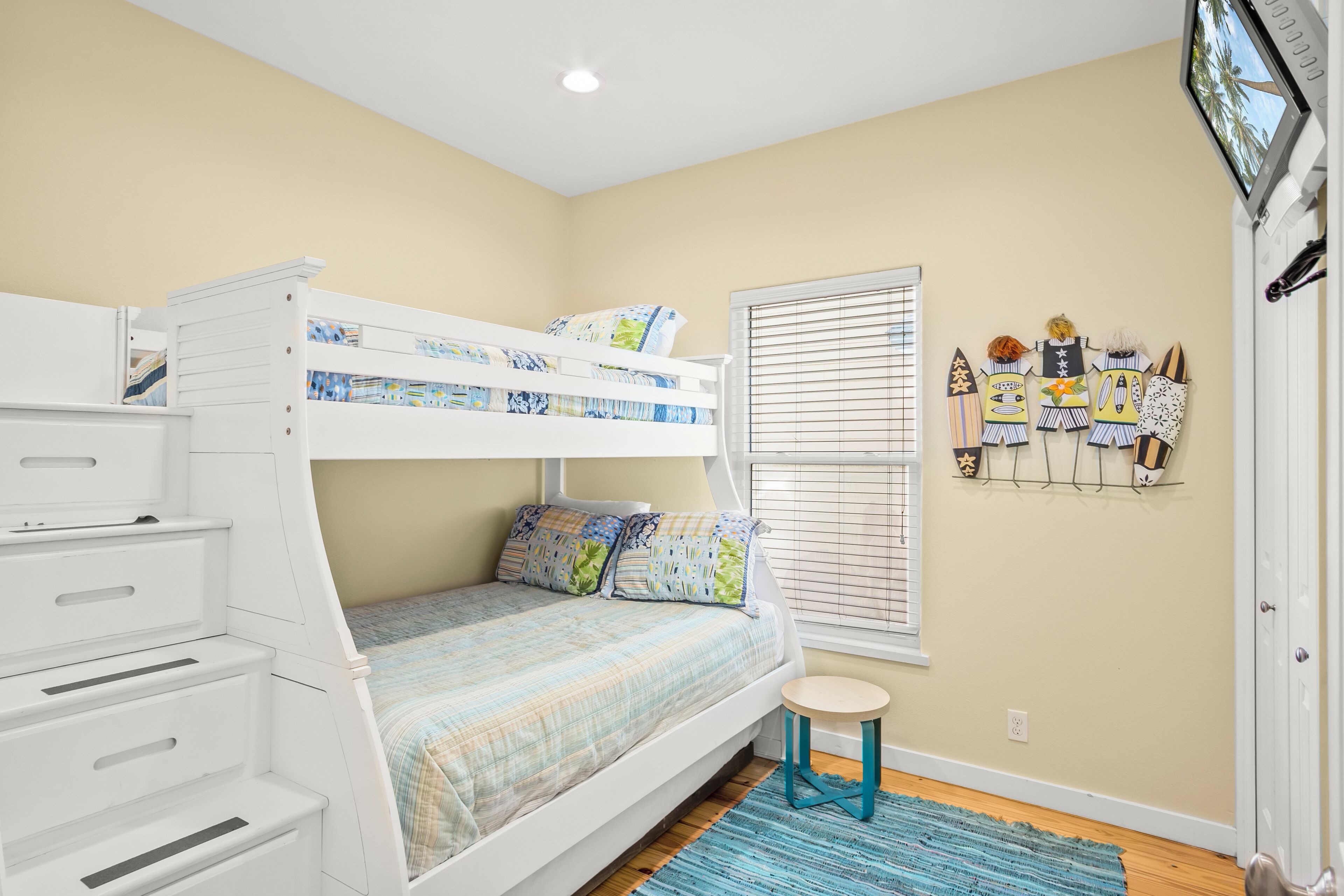 Una cama litera con cajones de almacenamiento, un taburete pequeño, una ventana con persianas y adornos en la pared.