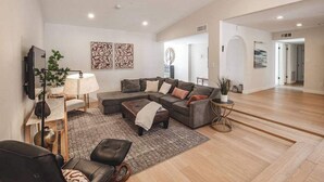 Un salon spacieux avec un canapé d’angle, une table basse, un téléviseur et une plante.