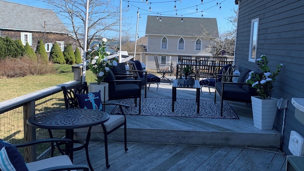 Une terrasse extérieure avec une plateforme en bois, des chaises et des tables en métal. Des guirlandes lumineuses sont suspendues au-dessus.