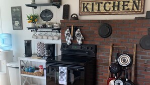 Une cuisine équipée d’une cuisinière, d’un four et de casseroles suspendues. On y trouve également un distributeur d’eau, une machine à café et un menu de café affiché au mur.