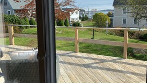 Une vue depuis une fenêtre donnant sur une terrasse en bois avec une balustrade, une pelouse et des maisons en arrière-plan.