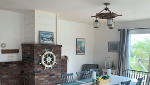 Un coin repas agrémenté d’une cheminée en briques, d’une décoration sur le thème de la marine et offrant une vue sur l’extérieur.